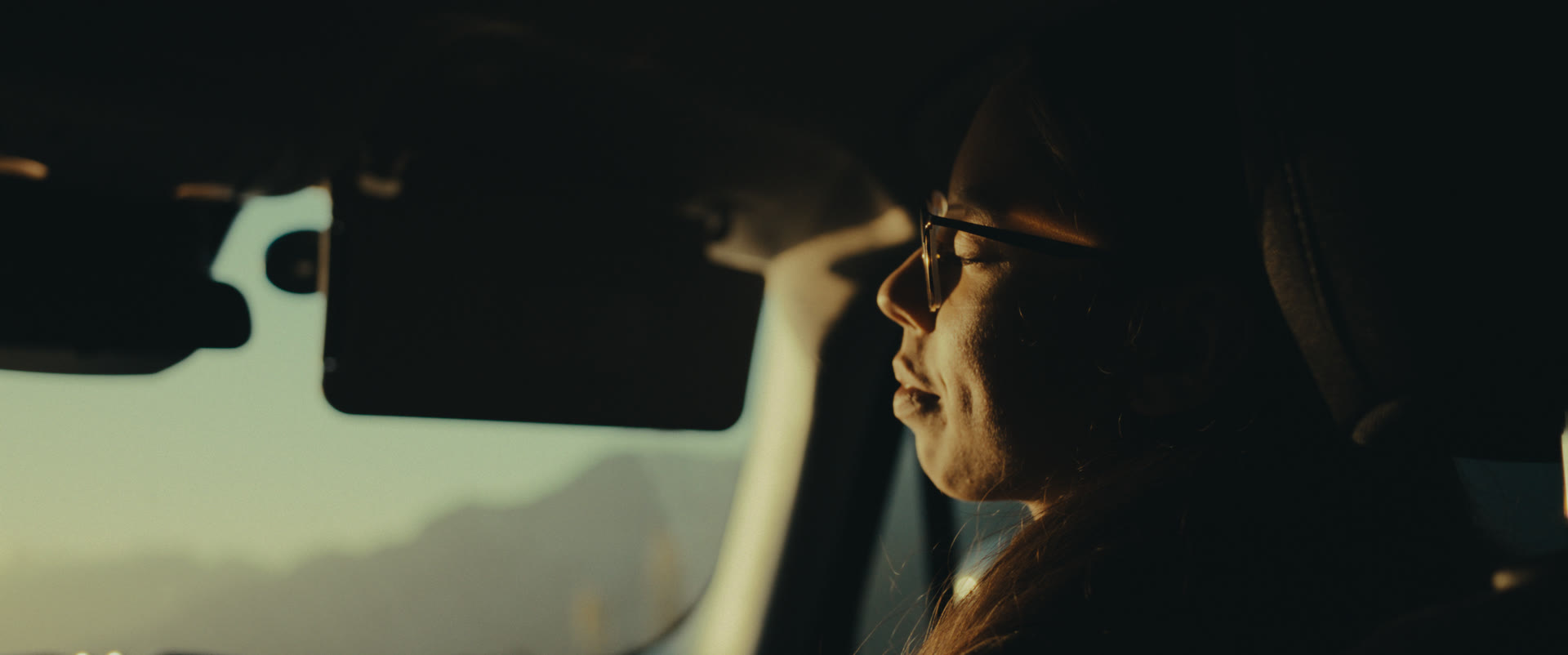 A woman smiles in the passenger seat, lit by low sun — still from Memories
