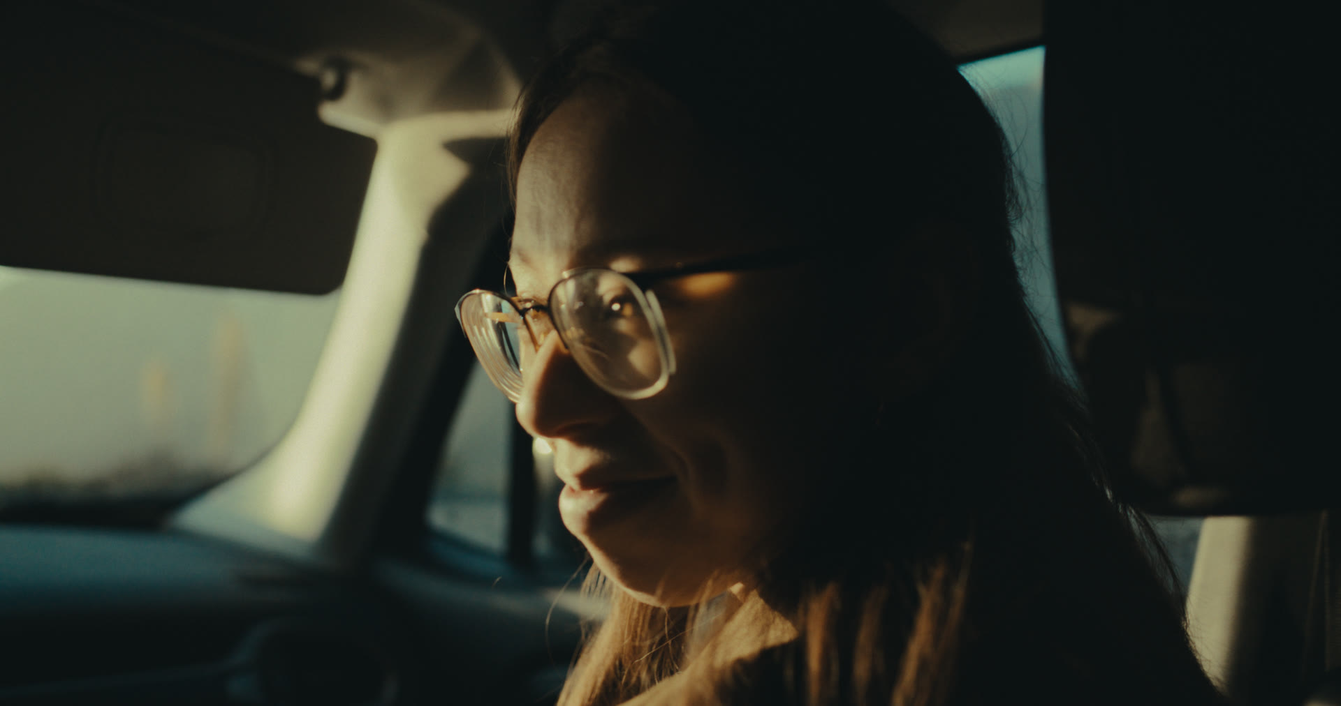 A woman smiles softly in golden hour light inside the car — still from Memories