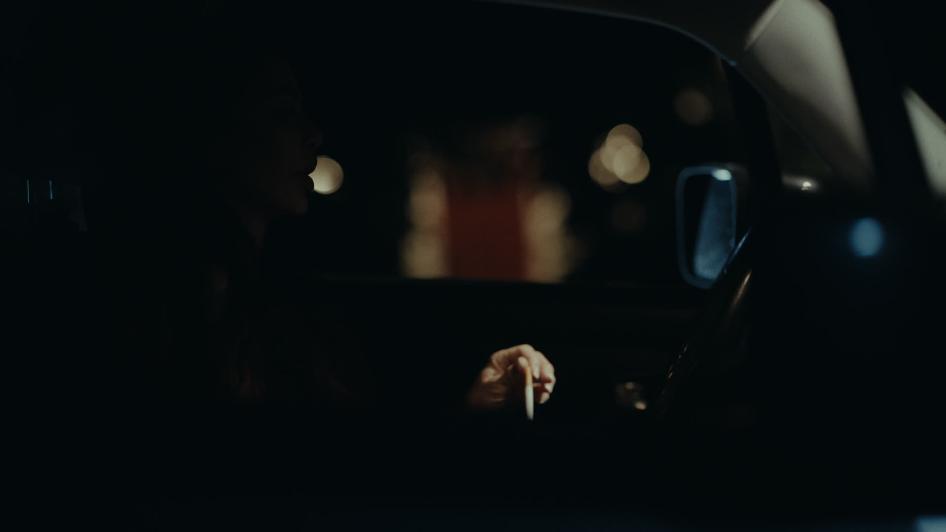 A woman lights a cigarette inside a parked car at night — still from Nobody Home