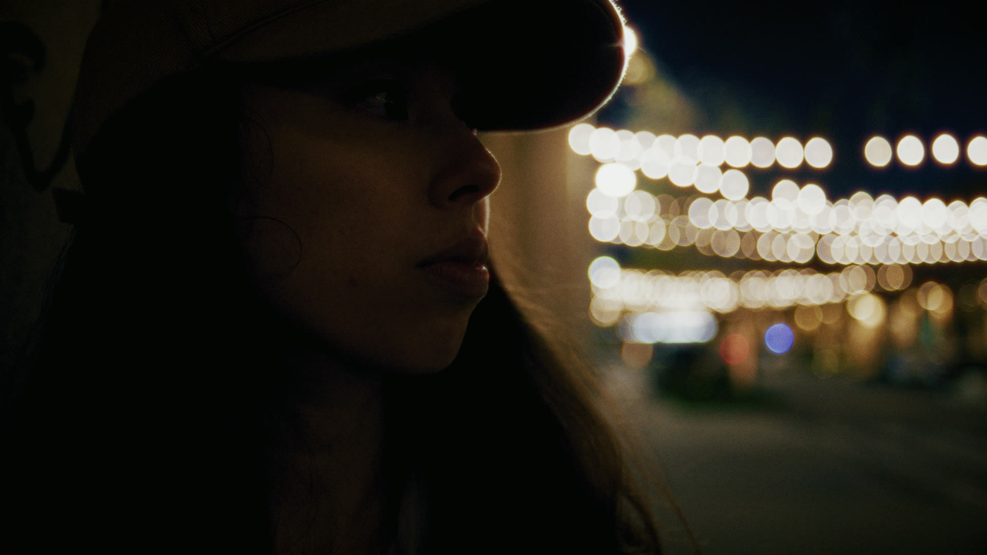 Profile close-up under strings of bokeh lights at night — still from The Row