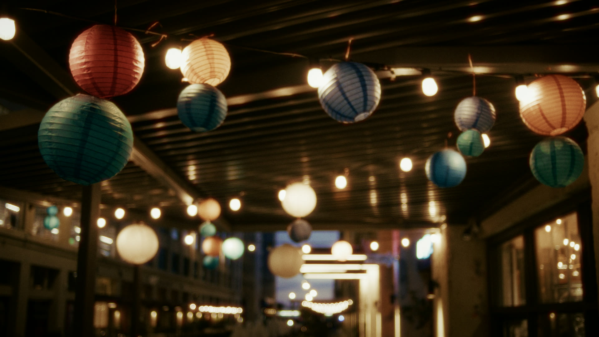 Paper lanterns strung above a patio at dusk — still from The Row