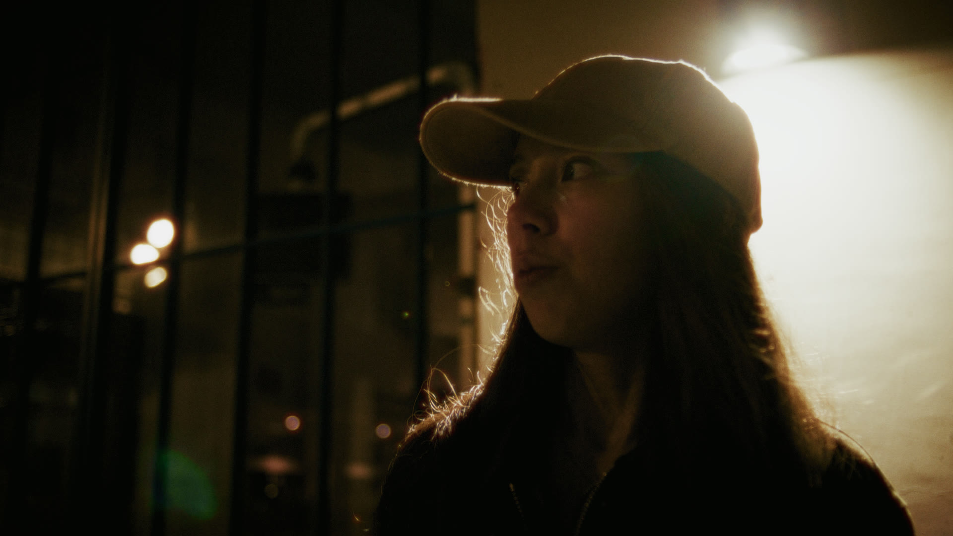 Backlit portrait in a ball cap at night — still from The Row