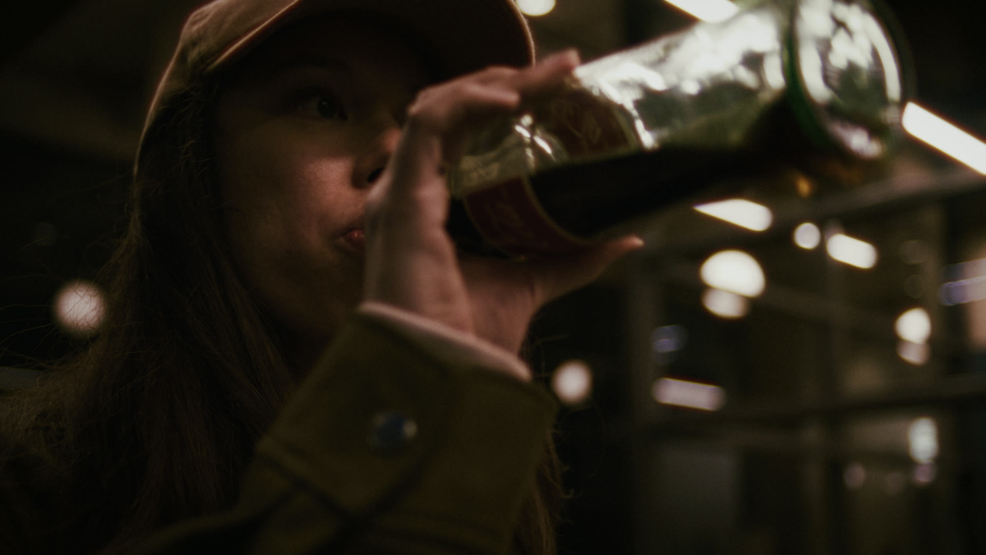 A woman drinks from a glass soda bottle under station lights — still from The Row