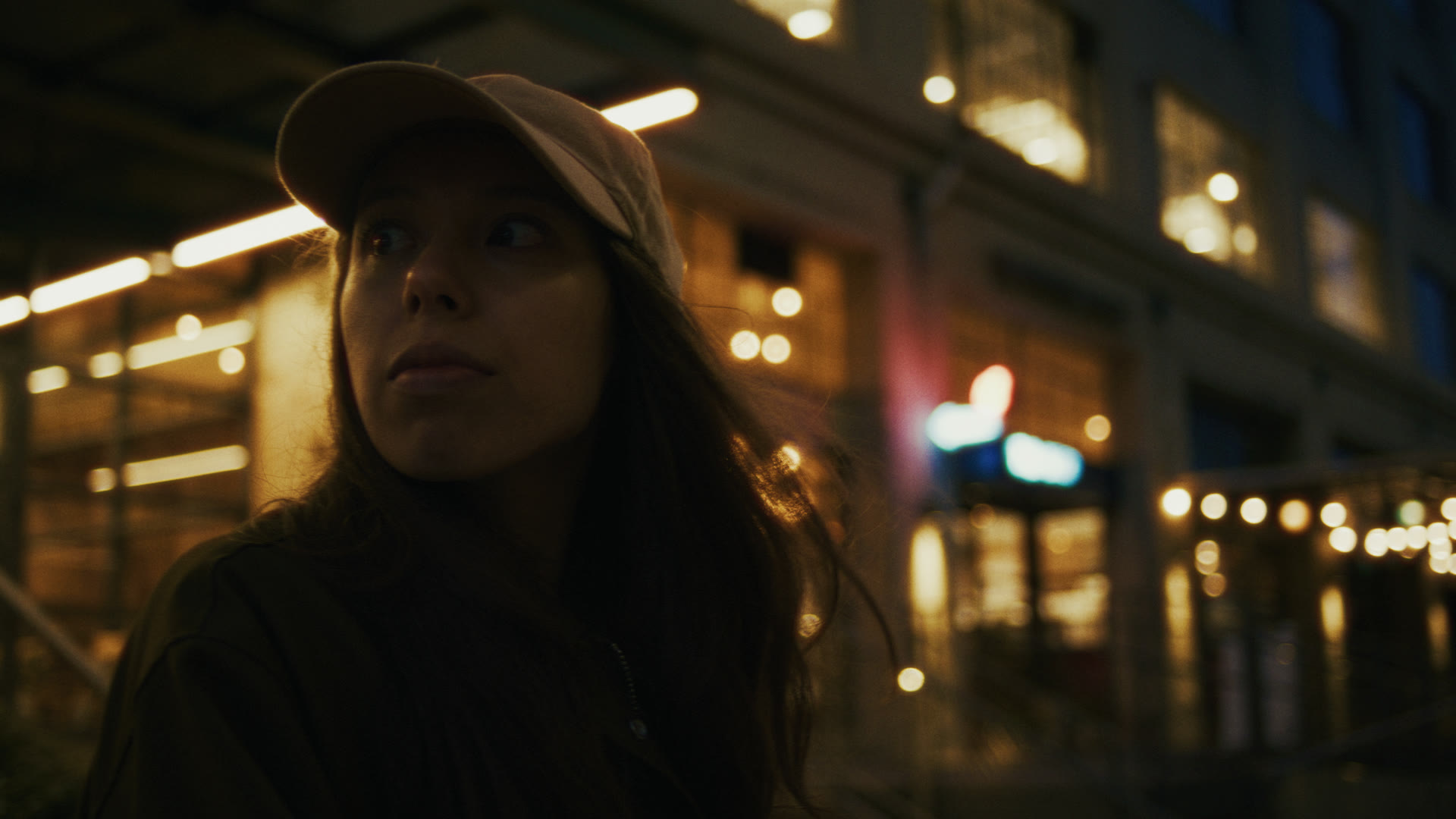 A woman looks off amid city lights at night — still from The Row