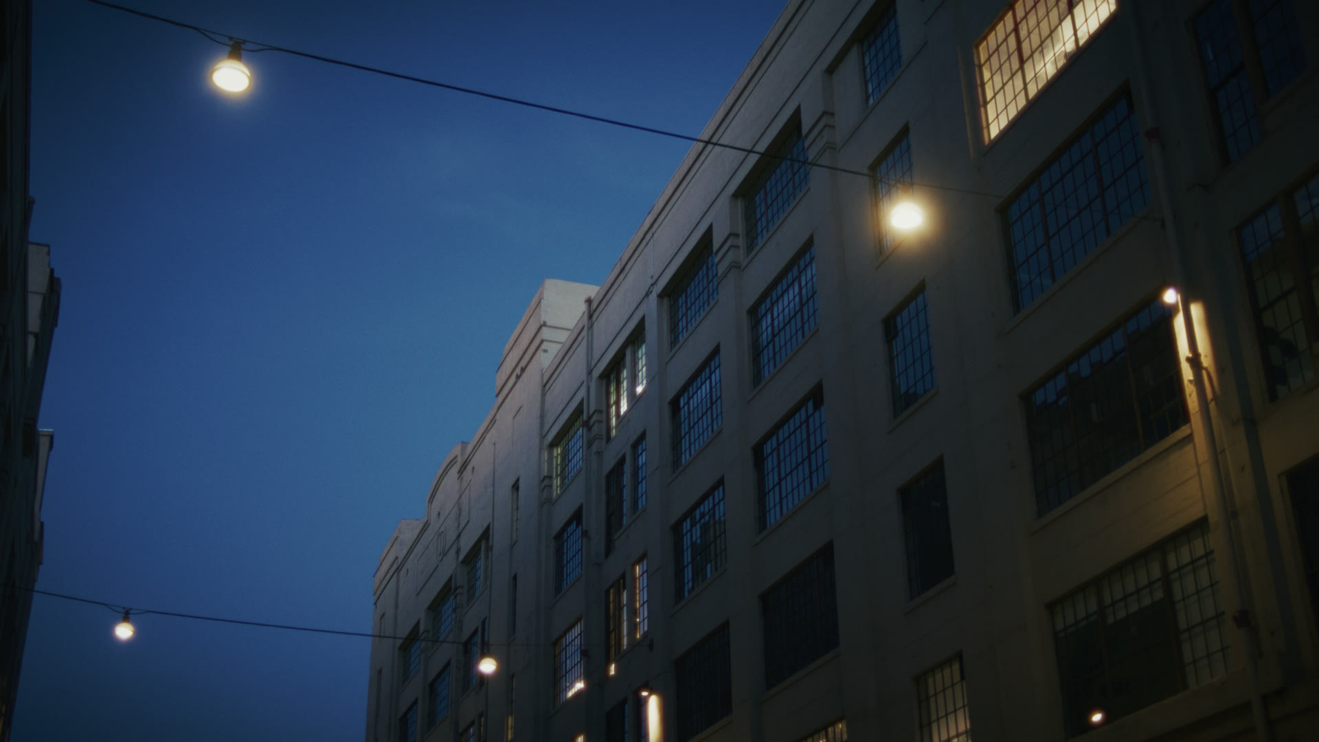 Industrial building exterior at dusk with string lights — still from The Row